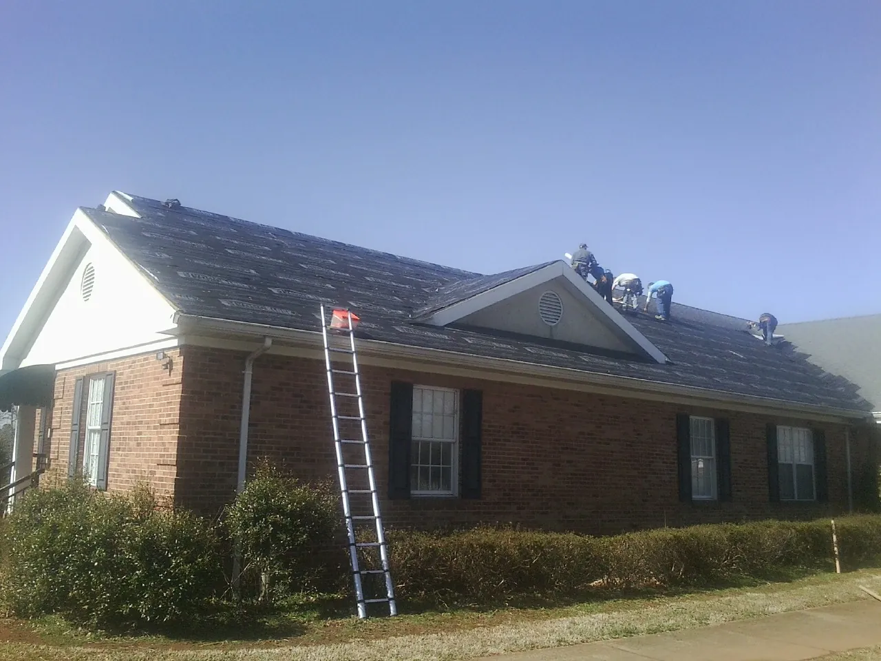 Crew tearing shingles off a brick ranch roof with a ladder set — Metal Roof Repair work by our crew in Manchester Township