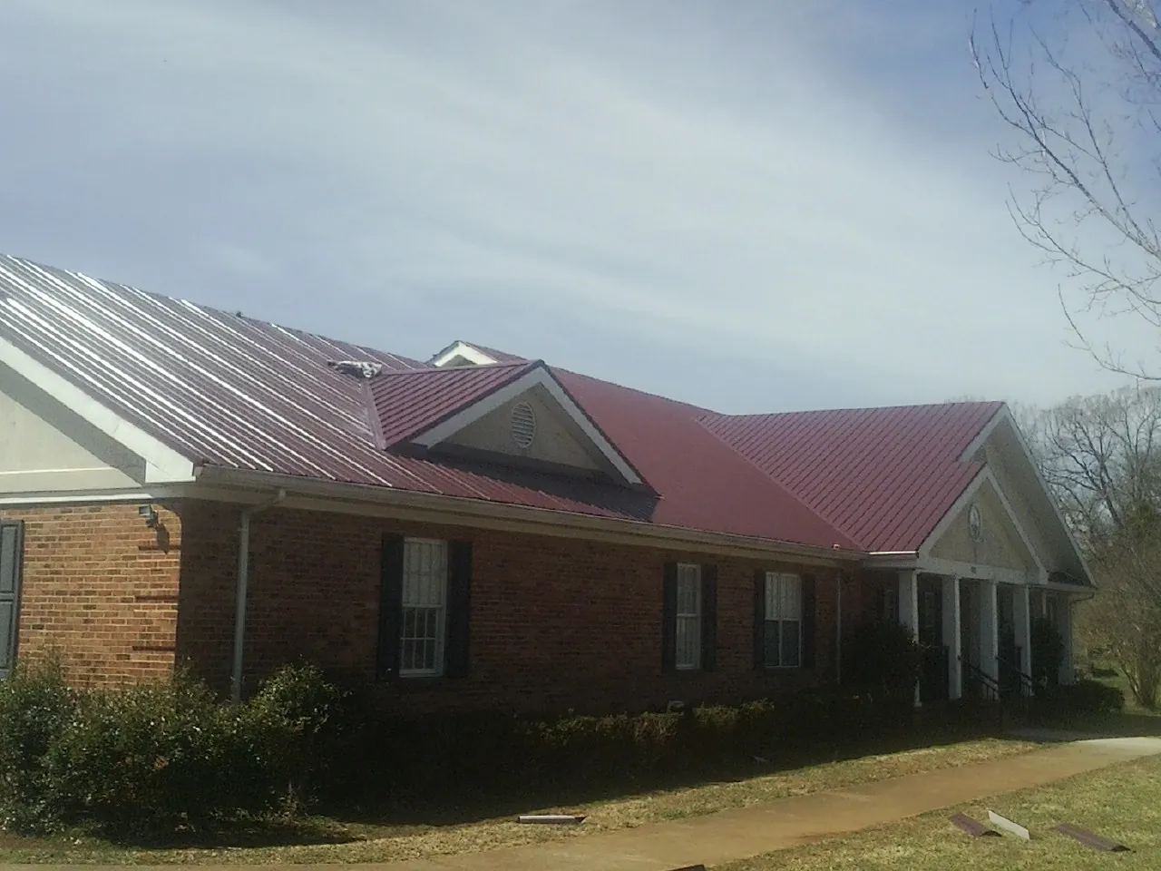 Red metal roof with gabled entries on a long brick building, from a Hail Damage Roof Repair job in Manchester Township
