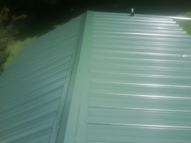 New green metal panels meeting at the ridge of a roof — Flat Roof Repair work by our crew in Manchester Township