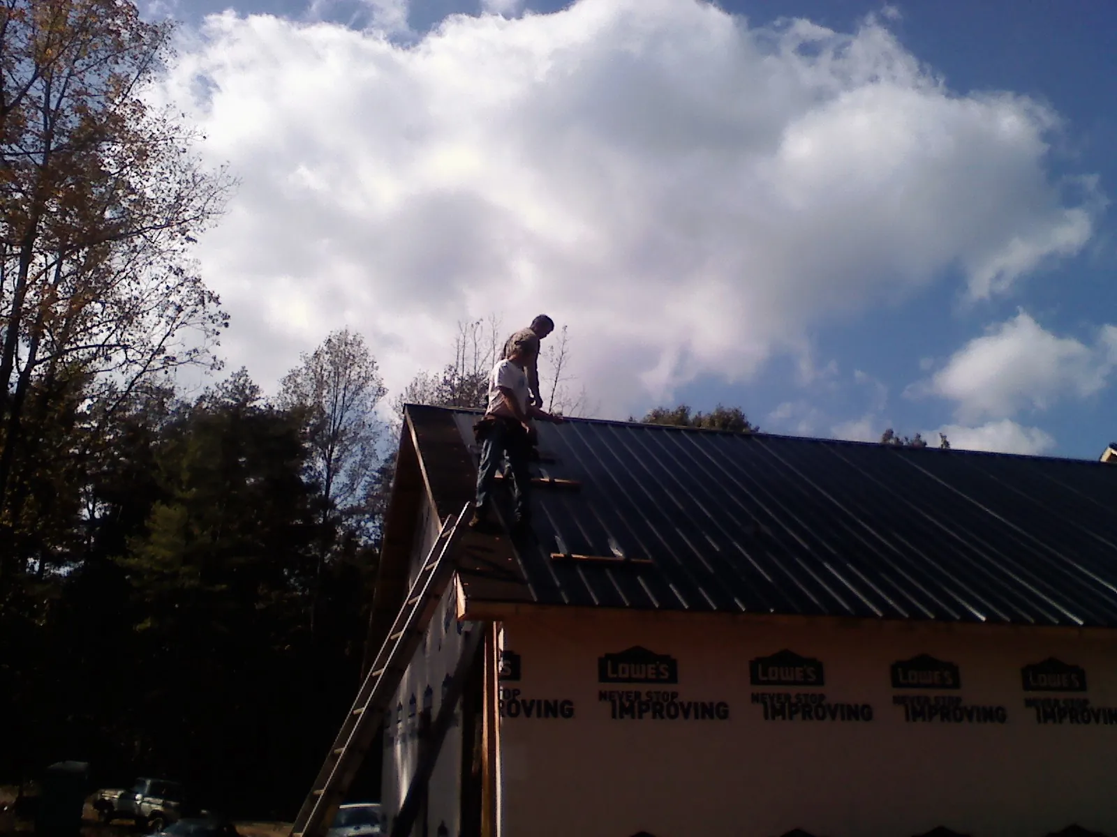 Roofer fastening dark metal panels high against a cloudy sky, from a Roof Inspection job in Manchester Township