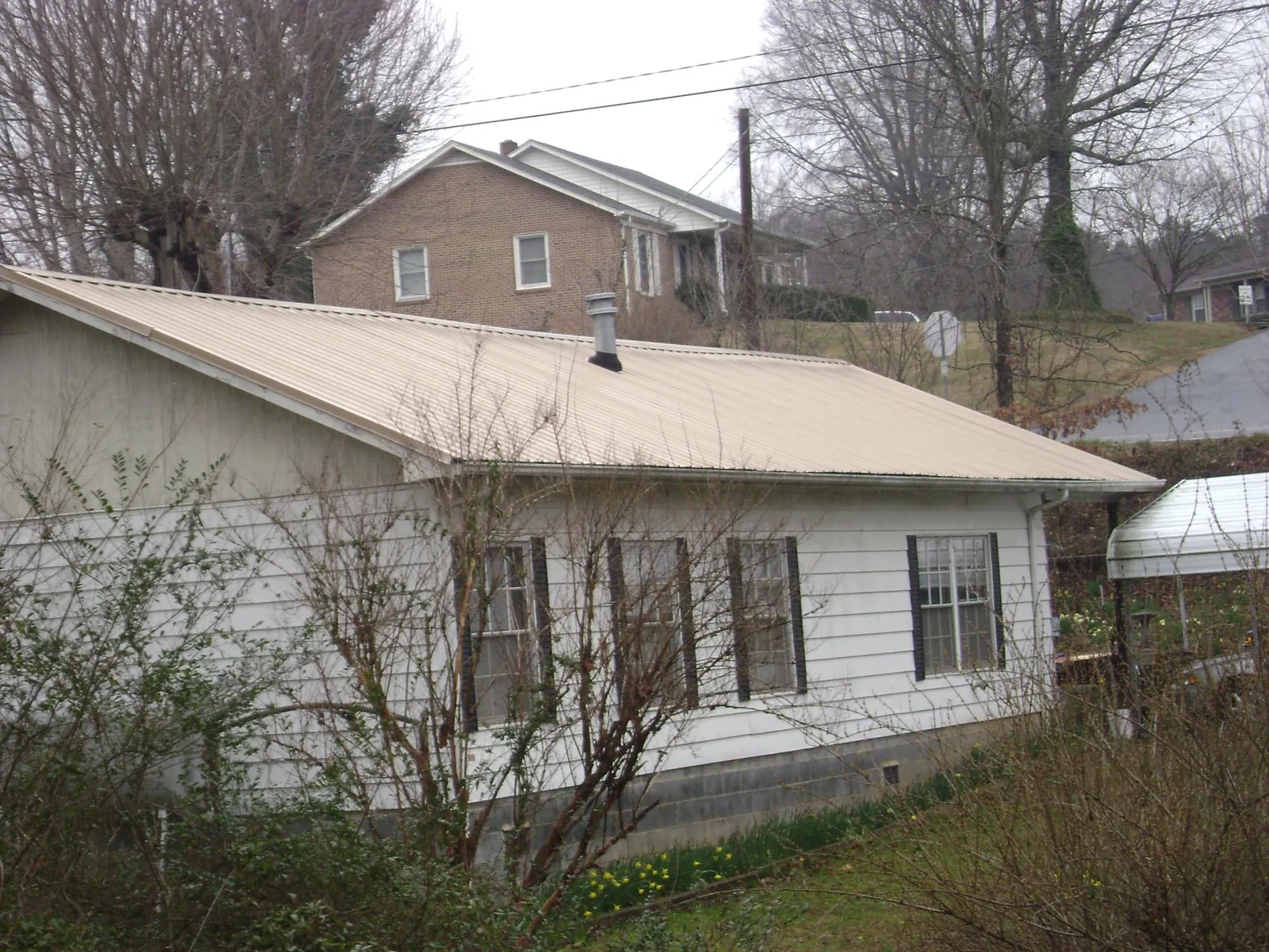 Tan metal roof on a white sided house set into a hillside — Commercial Roofing by Roofing Brothers in Manchester Township